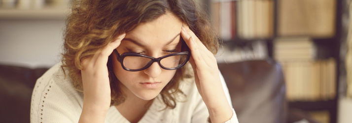 A woman with glasses resting her fingers on her temples