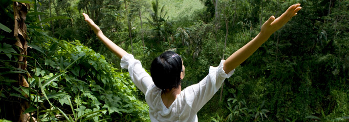 A person raising both arms beside a wooded path